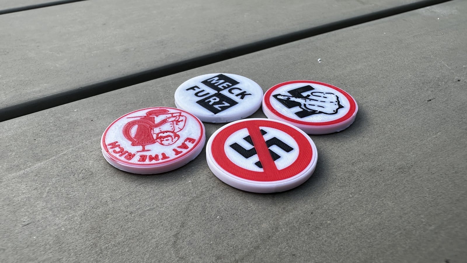 Vier 3D-gedruckte Einkaufswagenchips auf Beton: Eat the Rich, MECK-FURZ, Fuck Nazis und Nazis Verboten